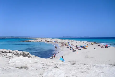 Gente disfrutando de un día soleado en las **playas blancas** con aguas turquesas y cielo azul.