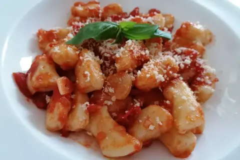 Pyszne gnocchi z sosem pomidorowym, posypane parmezanem i udekorowane listkiem bazylii.
