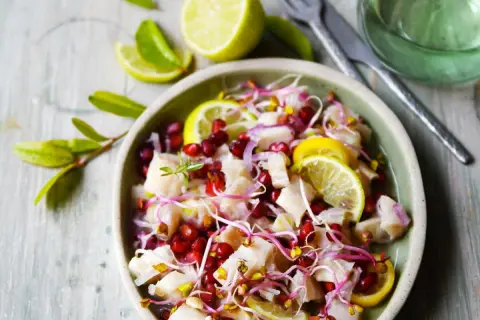 Un délicieux ceviche de poisson frais, garni de grenade, de pousses et de rondelles de citron vert.