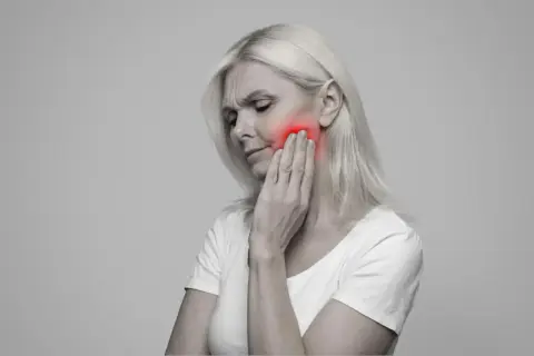 Donna con dolore alla mascella, evidenziato in rosso. Le conseguenze di una mandibola fuori asse possono essere debilitanti.