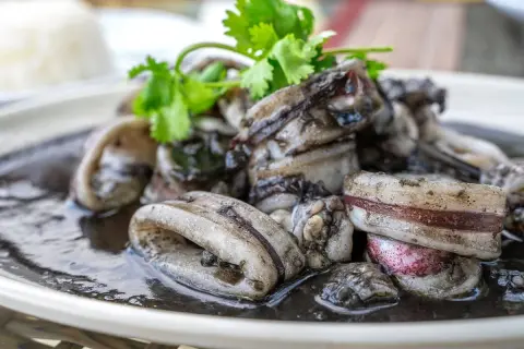 Calamares en su tinta, un plato oscuro y delicioso, adornado con cilantro fresco.