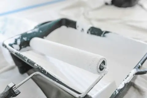 Un rouleau à peinture blanc est posé dans un bac en plastique noir, prêt à enlever la peinture.