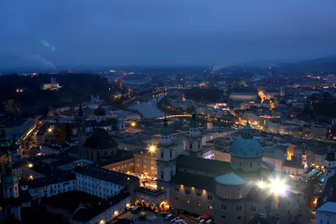 Salzburg im Winter bei Nacht. Lichter der Stadt, die Salzach und die Festung Hohensalzburg erhellen die Szene.