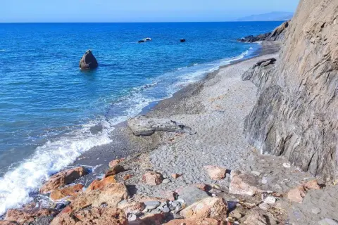 Costa de Almería, con sus guainos y rocas, el mar azul y las olas rompiendo en la playa de guijarros.