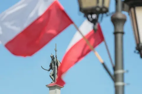 Pomnik rycerza z mieczem i krzyżem na tle polskich flag i latarni.