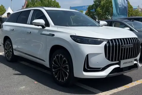 Biały SUV Jaecoo J9 z chromowanym grillem i czarnymi felgami stoi na parkingu.