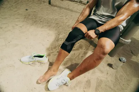 Un athlète ajuste sa genouillère TFL Decathlon sur un terrain sablonneux, prêt pour son entraînement.