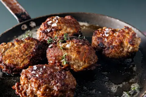 Saftige vegetarische Frikadellen braten in einer Pfanne, bestreut mit grobem Salz und frischem Thymian.