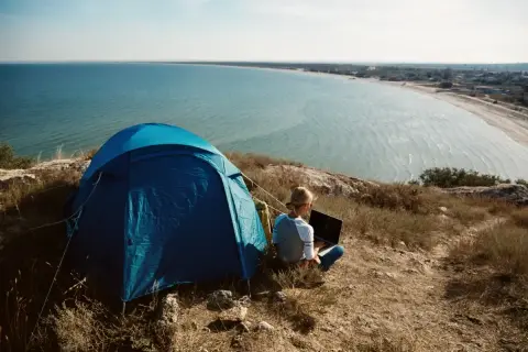 Niebieski namiot i osoba z laptopem na wzgórzu, z widokiem na morze i wybrzeże. Idealne miejsce na camping na Lazurowym Wybrzeżu.