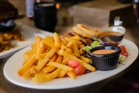 Chrupiące frytki z piekarnika, idealne na lekki posiłek. Zastanawiasz się nad ich kcal? Podane z sosem i sałatką.