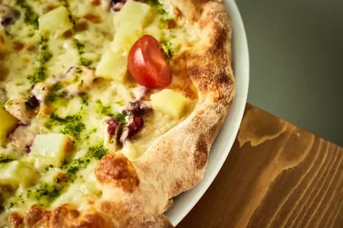 Pyszna pizza z kawałkami ananasa, ośmiornicy i pomidorkiem, obficie posypana zielonym pesto i roztopioną **mozzarellą w bloku**.