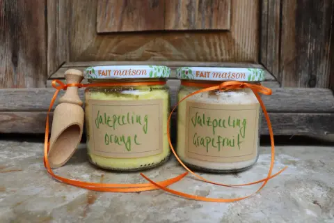 Zwei Gläser mit selbstgemachtem Saunasalz (Orange & Grapefruit) und eine Holzschaufel, verziert mit orangefarbenen Bändern.
