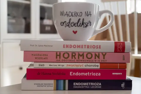 Stos książek o endometriozie, w tym "Endometrioza: diagnostyka i leczenie", z kubkiem "Wiaderko na endoeliksir".