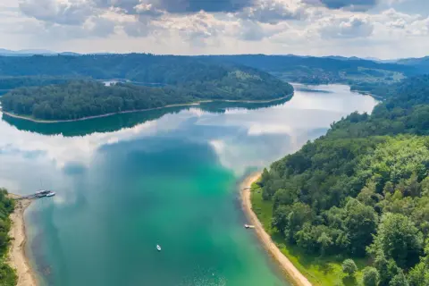 Malownicze jezioro otoczone lasami, z łodziami przy brzegu. To jedne z pięknych atrakcji przyrodniczych w Polsce, idealne na wypoczynek.