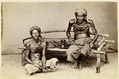 Dos hombres demacrados, víctimas de la guerra del opio, sentados con pipas de opio.