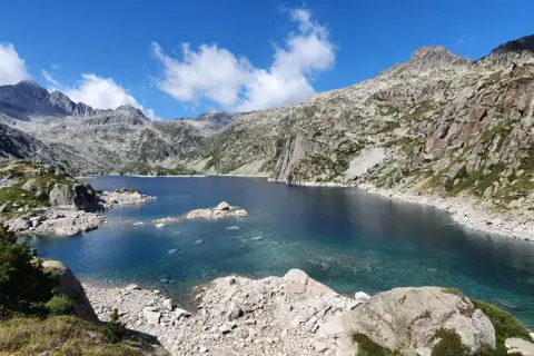 Lago azul cristalino en el corazón del Vall de Boí Aigüestortes, rodeado de imponentes montañas rocosas y vegetación escasa.
