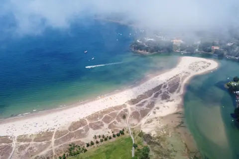 Vista aérea de la playa y la ría de Miño. Un día soleado con gente disfrutando de la arena y el mar. ¡Descubre qué ver en Miño!