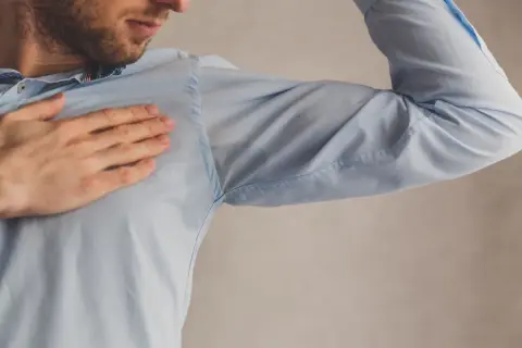 Hombre con camisa azul mostrando manchas de sudor bajo el brazo. Una solución para quitar manchas de sudor es necesaria.