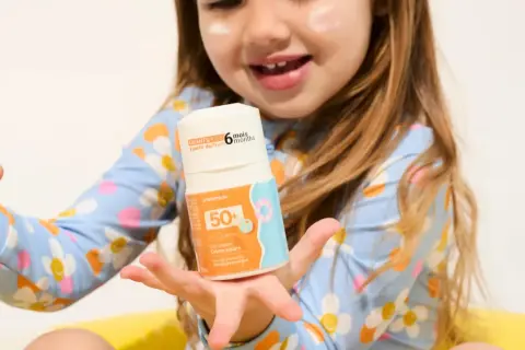 Un enfant tient un flacon de crème solaire UVA UVB 50+. La crème est conçue pour les enfants dès 6 mois.