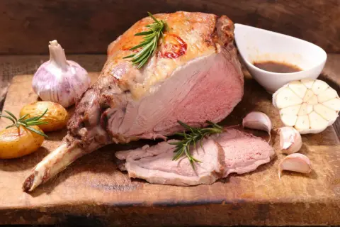 Ein saftiger Lammbraten, perfekt für Ostern, mit Rosmarin, Knoblauch und kleinen Kartoffeln auf einem Holzbrett.
