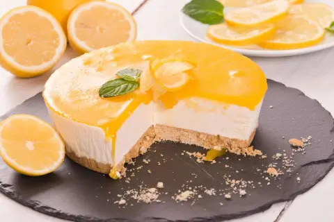 Ein Anschnitt eines cremigen Lemon Cheesecake mit Zitronenscheiben und Minze garniert.