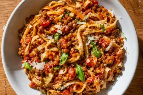 En skål med vegetarisk pasta med linser, tomatsås och basilika, toppad med riven ost.
