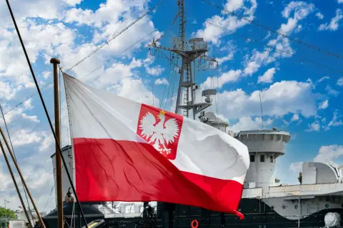 Flaga bandery z orłem dumnie powiewa na tle błękitnego nieba z chmurami, nad pokładem statku.