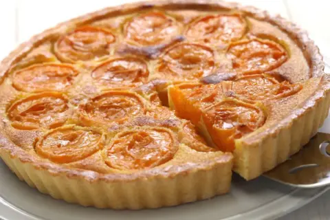 Une délicieuse tarte aux abricots, avec une part déjà servie, révèle sa garniture dorée et ses fruits juteux.