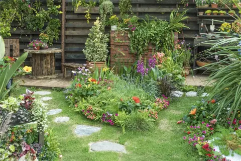 Un jardín exuberante y colorido, con flores vibrantes, follaje verde y un camino de piedras. El mantenimiento de jardinería es clave para esta belleza.