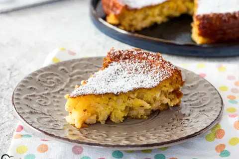 Una fetta di torta di riso, la ricetta della nonna, cosparsa di zucchero a velo su un piatto grigio.