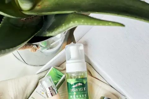 Mousse limpiador facial de aloe vera cosmetica, con planta de aloe vera y envases de productos de belleza.