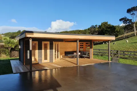 Modern cabin with porches cerrados de obra, deck, and outdoor seating, set against a green hillside with sheep.