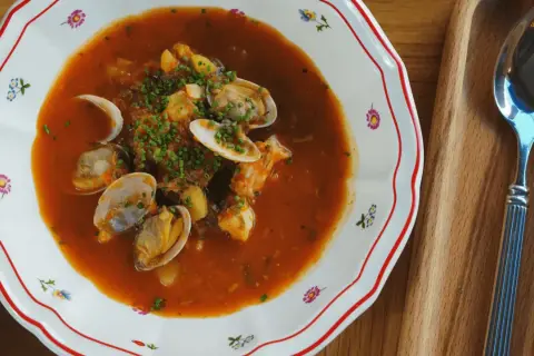 En skål med bouillabaisse med musslor och räkor, perfekt att servera med ett glas vin.