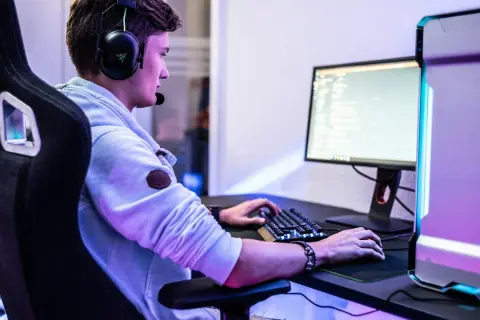 Ein junger Mann mit Headset spielt am PC. Er fragt sich vielleicht, was bedeutet gg im Chat.
