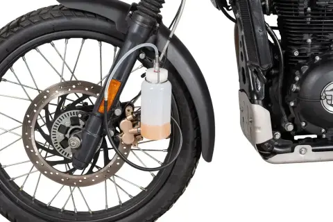 Zbiorniczek z płynem do odpowietrzania hamulców motocykla, podłączony do zacisku hamulcowego przy przednim kole.