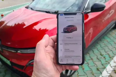 Aplikacja na telefonie pokazuje, jak przerobić auto na elektryczne, obok czerwonego samochodu.