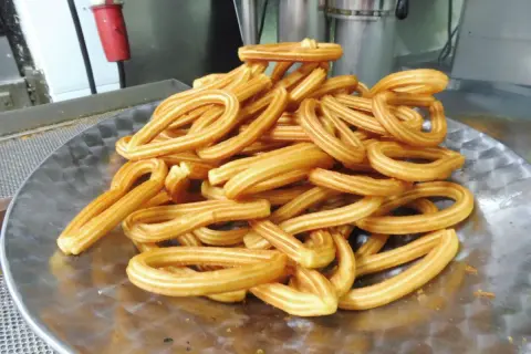 Montón de churros dorados en forma de lazo sobre un plato metálico.