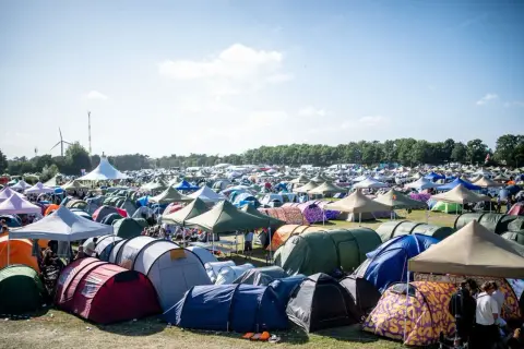 Ein Meer von Zelten beim Roskilde Festival. Menschen entspannen sich im Freien unter blauem Himmel, umgeben von bunten Unterkünften.