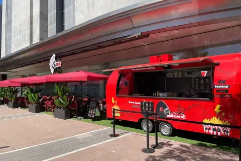 Food truck rojo "Puro Goxis" de Dabiz Muñoz, con "Mamma!!!" y "Alta cocina callejera!!" escrito. Mesas y sombrillas rojas al lado.