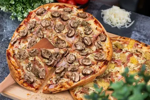 En härlig liba pizza med champinjoner och skinka, redo att avnjutas. Bredvid ligger en annan pizza med ananas och skinka.