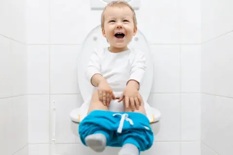 Bambino felice sul water, pantaloni abbassati, pronto per la sua prima cacca nel water.