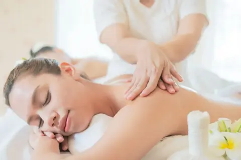 Mani esperte mostrano come fare un massaggio alla schiena rilassante, con fiori di plumeria e un sacchetto di erbe.