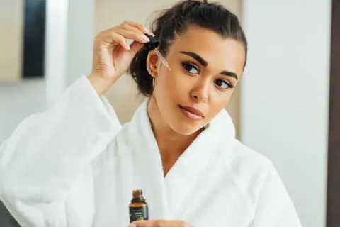Une femme applique un sérum sur son visage, peut-être un mélange d'acide azélaïque et de vitamine C, pour une peau éclatante.