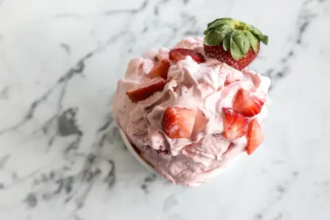 Un délice rose et crémeux : un sorbet fraise garni de morceaux de fruits frais et d'une fraise entière sur un fond marbré.
