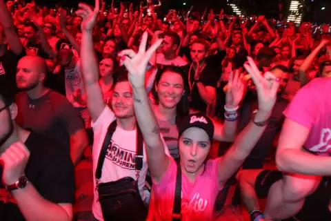 Tłum na koncercie Armin van Buuren Polska, fani pozdrawiają DJ-a, czerwone światła tworzą energetyczną atmosferę.