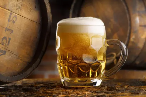 Boccale di birra dorata con schiuma, accanto a botti di legno. Un litro di birra calorie da gustare con moderazione.