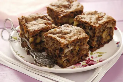 Vier Stücke saftiger Apfel Walnuss Kuchen auf einem Teller mit floralem Muster, daneben eine antike Kuchenzange.