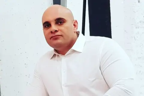 Dominik Abus, wiek nieznany, w białej koszuli, na tle białej ściany z czarnymi pasami.