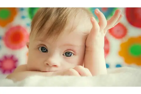 Bambino con sindrome di Down, occhi azzurri, mano sul viso. La vita delle persone Down è piena di amore e gioia.