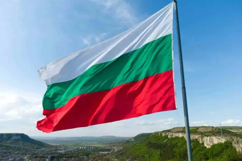 Flaga Bułgarii powiewa na tle błękitnego nieba nad malowniczym krajobrazem. Winieta Bułgaria.